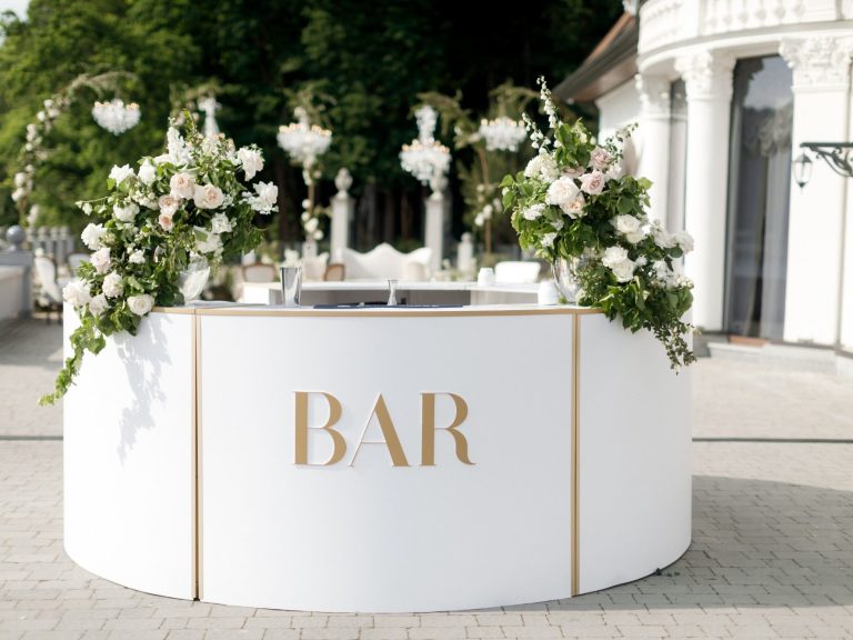 Elegant white bar with gold lettering, adorned with floral arrangements and greenery.